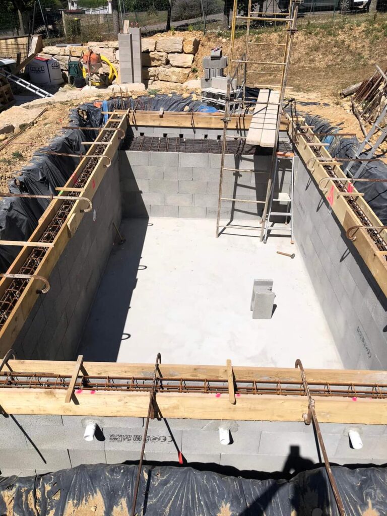 Construction Piscine : Murs en parpaings et chaînage prêt. Construction d'une piscine résidentielle : murs en parpaings, radier coulé. Armature et coffrage de chaînage installés, prêts pour le béton.