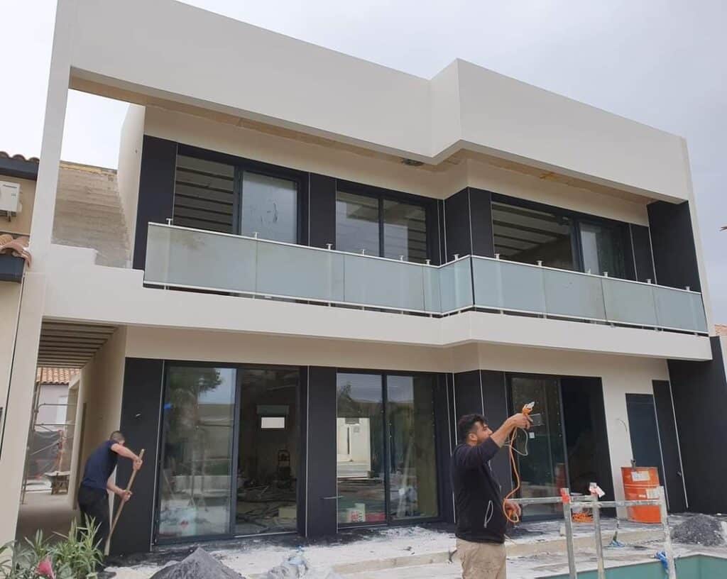 Maison moderne en construction : façade blanche et balcon vitré Construction d'une maison moderne minimaliste. La façade contrastée (noir/crème) présente un large balcon avec un garde-corps en verre.