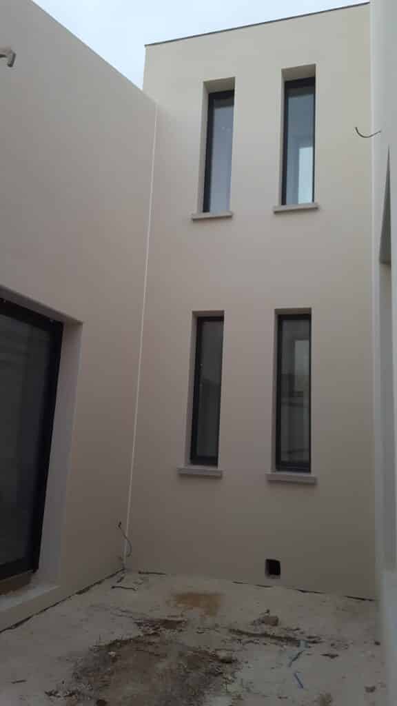 Façade beige moderne avec fenêtres étroites noires et sol en chantier. Architecture minimaliste contemporaine.
